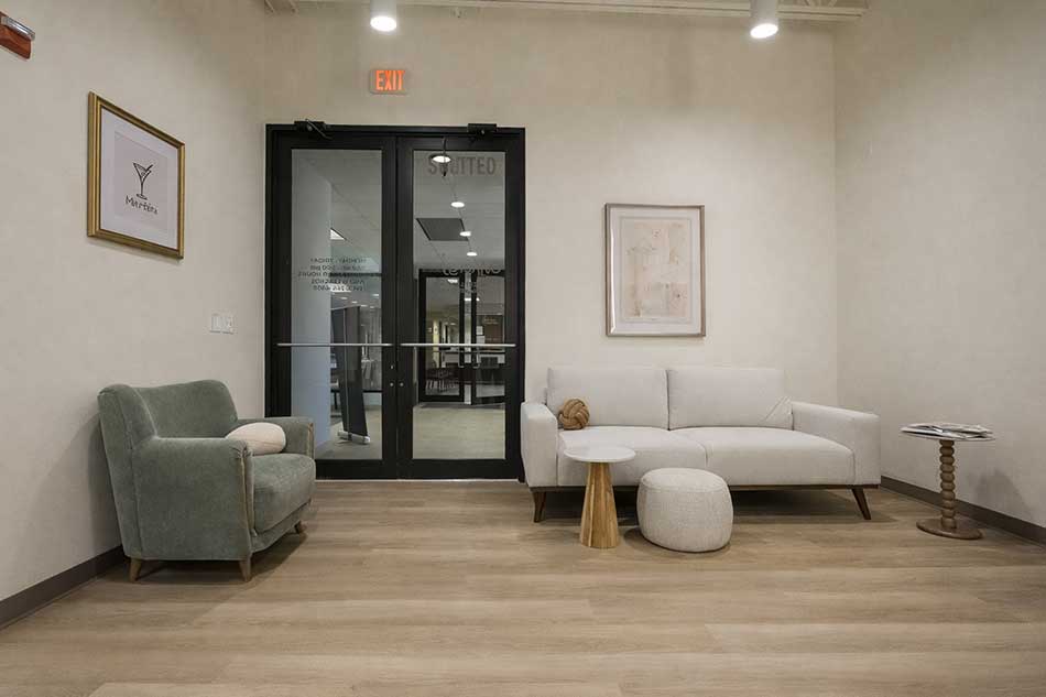 Synergy Health waiting area with sofa, chair, accent table, and modern office entry doors.